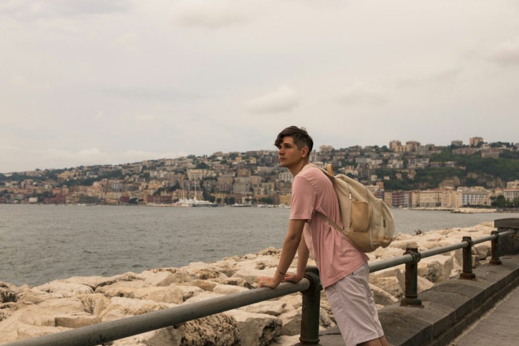 A young man leaning on a fence looking at the sea